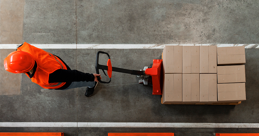 Profissional logístico movimentando pallets em armazém moderno, ilustrando eficiência operacional e gestão de estoque.